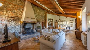 Un interior rústico con pared de piedra, vigas de madera, chimenea, sofá y zona de cocina.