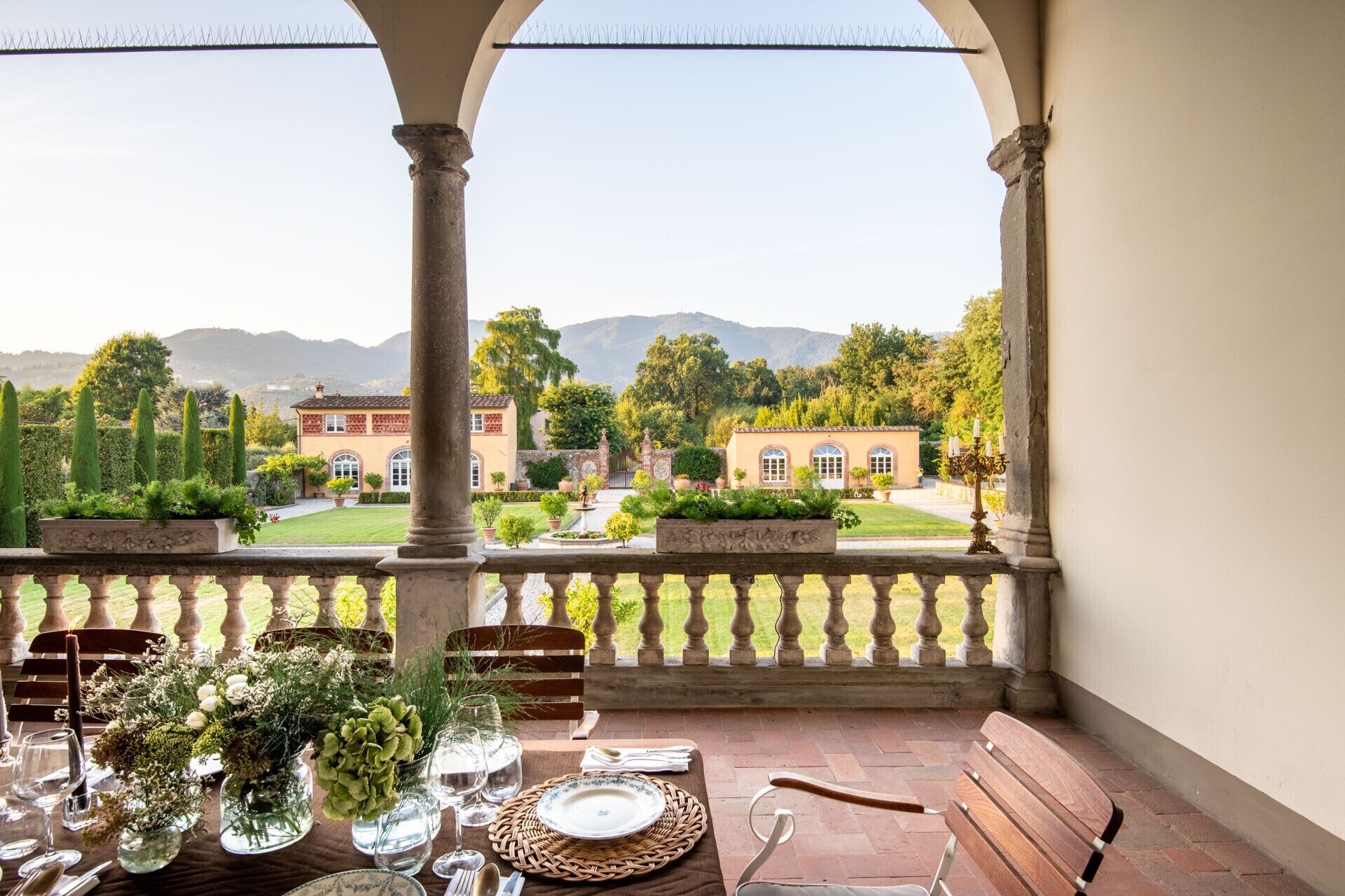 A terrace with a table set for dining, overlooking a landscaped garden and a distant mountain range.