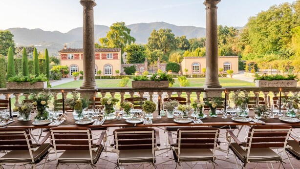 An outdoor dining area with tables set for a meal, overlooking a landscaped garden and distant buildings. - Air Conditioned 10 Bedrooms Luxury Villa and Pool in Lucca (Capannori)
