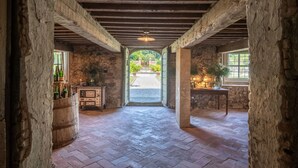 A rustic stone-walled room with a herringbone floor, wooden beams, and a view of a garden through an arched doorway. - Air Conditioned 10 Bedrooms Luxury Villa and Pool in Lucca (Capannori)