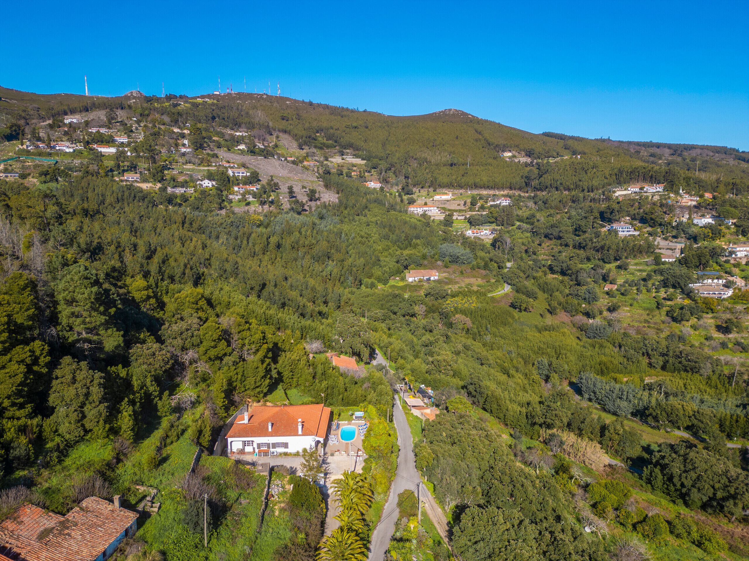 An aerial view of a residential area with houses, a swimming pool, and a hilly landscape.