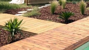 Eine Holzterrasse mit Bett und Baldachin, umgeben von Pflanzen und einem Pool.