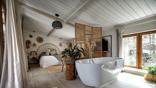 Ein geräumiges Schlafzimmer mit einer großzügigen Badewanne, Holzboden und einem großen Fenster mit Blick ins Freie.