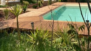 Ein Poolbereich mit Holzterrasse, überdachten Sitzgelegenheiten und üppiger Bepflanzung.