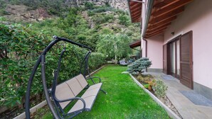 Un patio con una mecedora, un banco, un árbol pequeño y un edificio de techo inclinado.