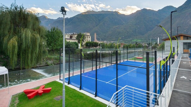 Una piscina azul al aire libre con valla, bancos rojos y vistas a montañas.