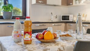 Una cocina con una mesa dispuesta para el desayuno, que incluye una cesta de frutas, botellas de leche y jugo, y una botella de agua.