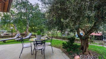 An outdoor patio with a table and chairs, a potted plant, and two lounge chairs.