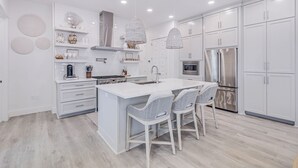 Una cocina moderna con armarios blancos, una isla central con taburetes y electrodomésticos de acero inoxidable.