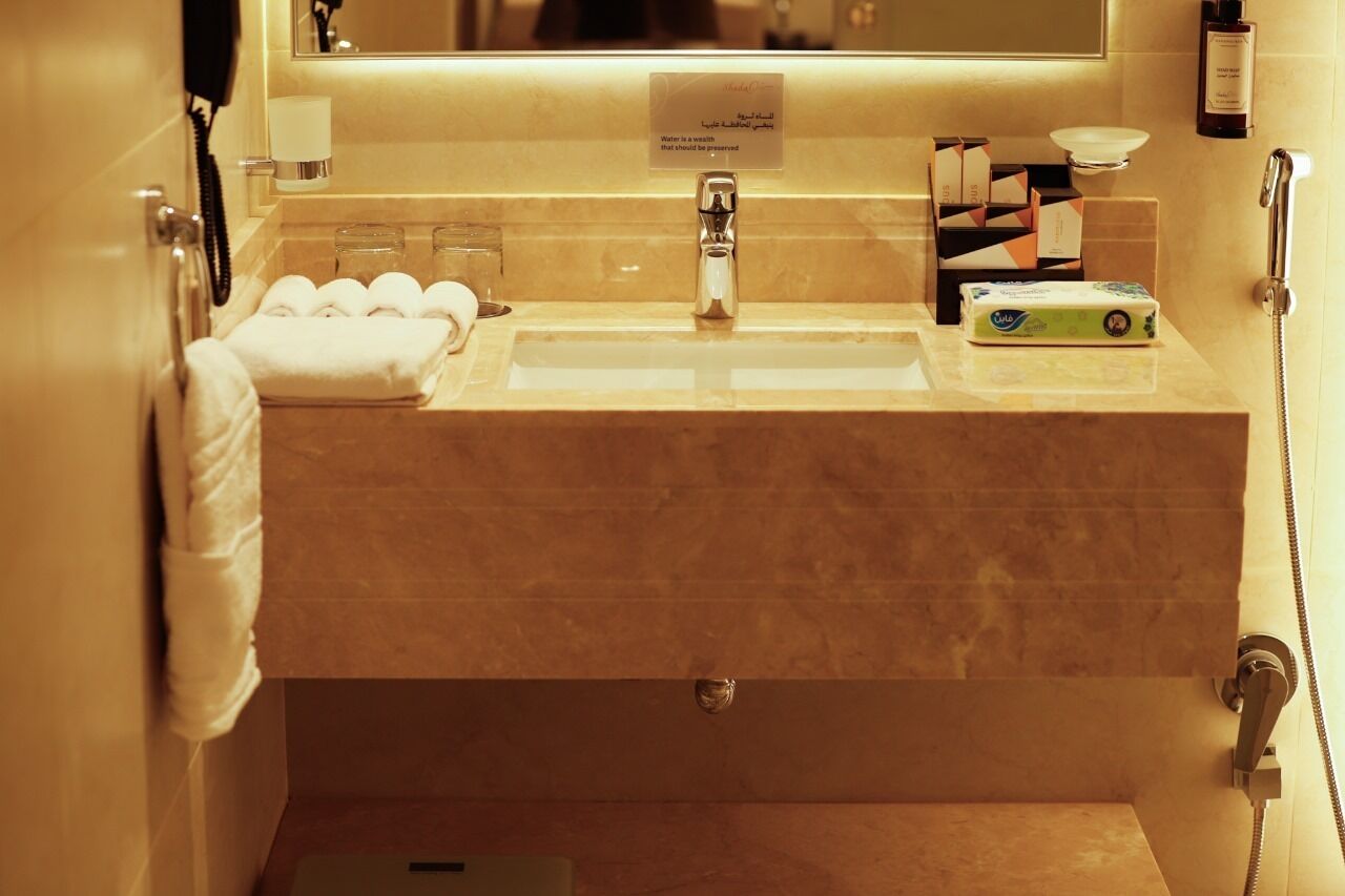 Baño de hotel con lavamanos, espejo, toallero y artículos de aseo.