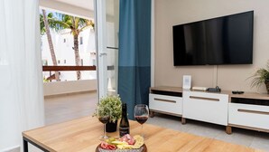 Un salon moderne avec une table à manger en bois, un téléviseur à écran plat fixé au mur et un balcon offrant une vue sur les palmiers.