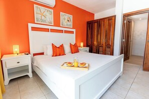 A bedroom with a bed, orange walls, wooden wardrobe, and a tray with breakfast. - Stunning Beachfront 3-BDR Apartment. STM L202 (BAVARO)