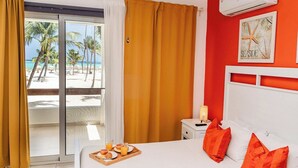 Une chambre d’hôtel avec un lit, des rideaux orange, une table de chevet, une lampe et un plateau de petit-déjeuner avec du jus d’orange et des croissants.