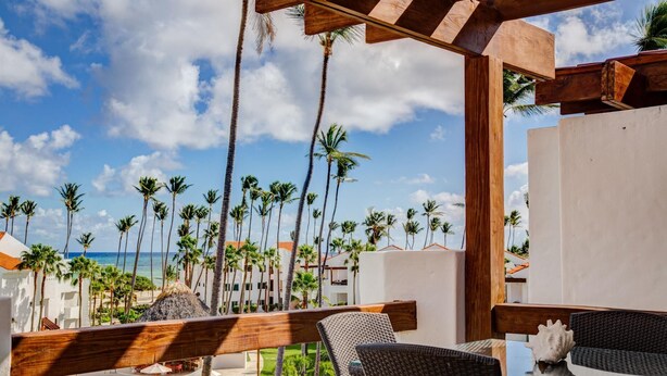 A poolside area with lounge chairs and a table, overlooking a beach with palm trees and a clear sky. - TesCosy Beachfront 2 BDR Apartment. STM G406 (BAVARO)