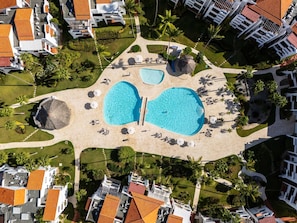 An aerial view of a resort with two large swimming pools, palm trees, and resort buildings.