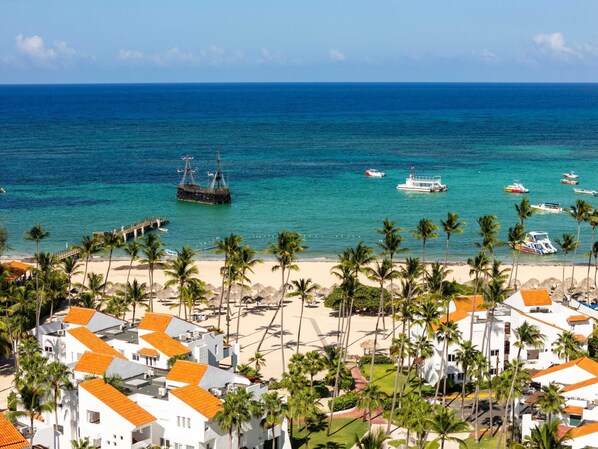 A coastal resort with white buildings, a sandy beach, and a clear blue sea.
