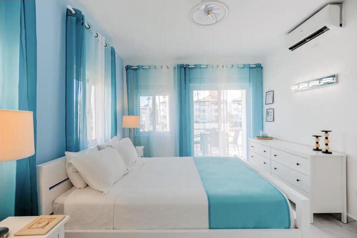 Ein Schlafzimmer mit Bett, Nachttisch, Kommode und einem Fenster mit Vorhängen.