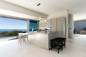 Una cucina moderna con una grande isola, un'area pranzo con sedie e vista sull'oceano.