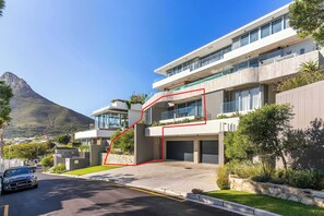 Un edificio moderno a più piani con garage, vialetto e una montagna sullo sfondo.