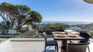 Una terraza con mesa y sillas, con vistas a un paisaje marino y vegetación.