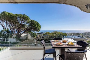 Eine Terrasse mit Tisch und Stühlen, mit Blick auf eine malerische Landschaft aus Meer und Grün.