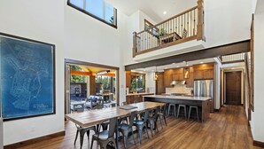 Una cocina amplia con techos altos, un comedor con una mesa grande y sillas, y vistas al exterior.