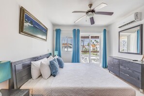 Een slaapkamer met een bed, een plafondventilator, een raam met gordijnen, een dressoir en een spiegel.