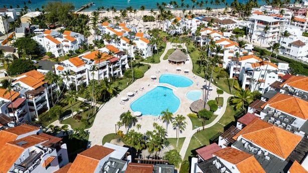 A resort with multiple buildings, a central pool area, and a beach with palm trees. - Room Mare F-302  Share  Save (BAVARO)