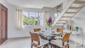 A dining area with a glass table, wicker chairs, a vase with flowers, a staircase, and a view of palm trees. - Room Mare F-302  Share  Save (BAVARO)