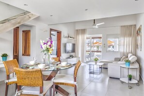 A modern living room with a dining area, a sofa set, a TV, and a balcony with a view.