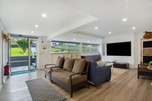A modern hotel room with a sofa, a television, a dining table, and a view of the outdoors. - Villa 'Quintinha Das Achadas' with Sea View, Private Garden and Wi-Fi (Achadas da Cruz)