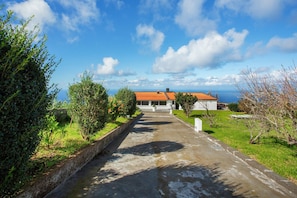 A pathway leading to a building with a red roof, surrounded by greenery and a clear sky. - Villa 'Quintinha Das Achadas' with Sea View, Private Garden and Wi-Fi (Achadas da Cruz)