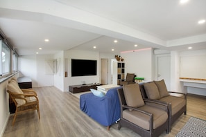 A spacious living area with a large flat-screen TV, wicker furniture, and a bookshelf. - Villa 'Quintinha Das Achadas' with Sea View, Private Garden and Wi-Fi (Achadas da Cruz)
