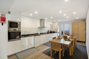 A modern kitchen with built-in appliances, a dining area with a wooden table and chairs, and a view of the outdoors. - Villa 'Quintinha Das Achadas' with Sea View, Private Garden and Wi-Fi (Achadas da Cruz)