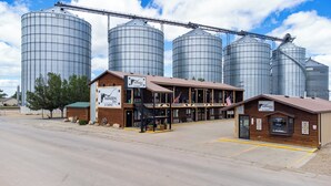 A Hansen Inn & Cabins building with a wooden exterior, located in front of large grain silos. - 8-Hansen Inn & Cabins, Room, Double Queen, Second Floor, No Pets, No Smoking (Wall)