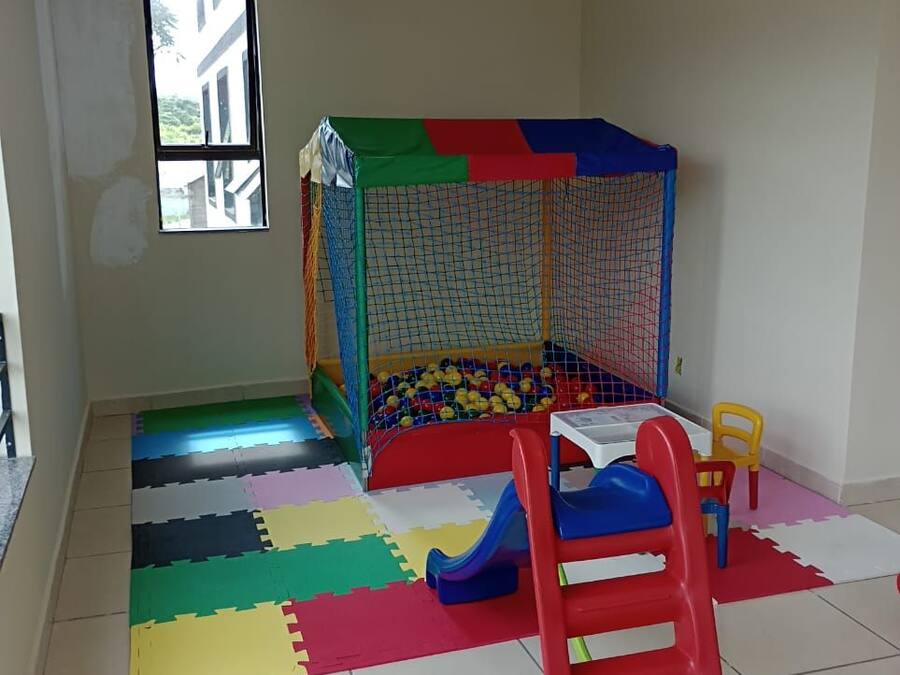 Uma área de recreação com piscina de bolinhas e escorregador, cercada por tapetes de espuma coloridos.