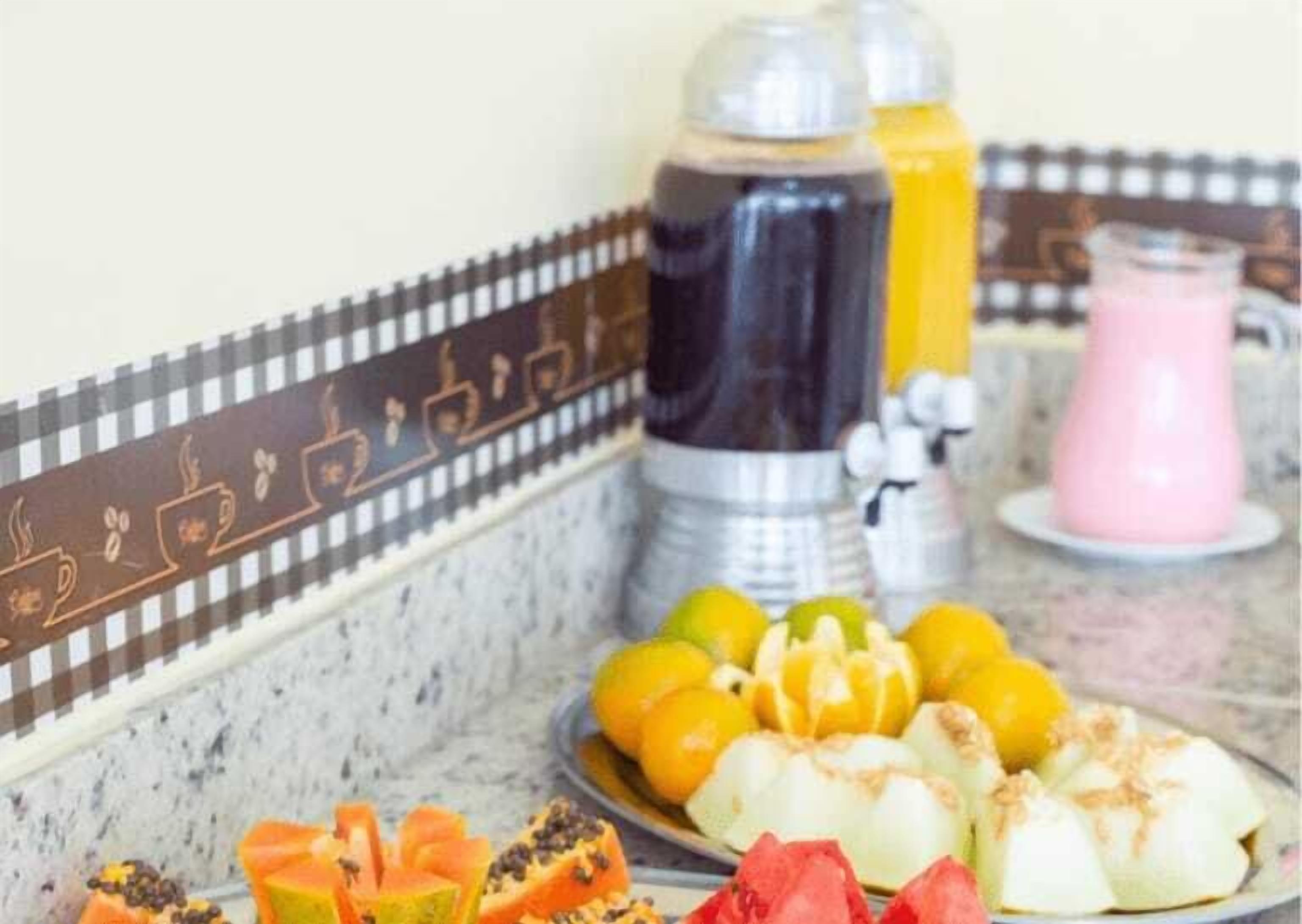 A kitchen counter with a coffee maker, a blender, and a pink drink. There are sliced fruits on the counter.