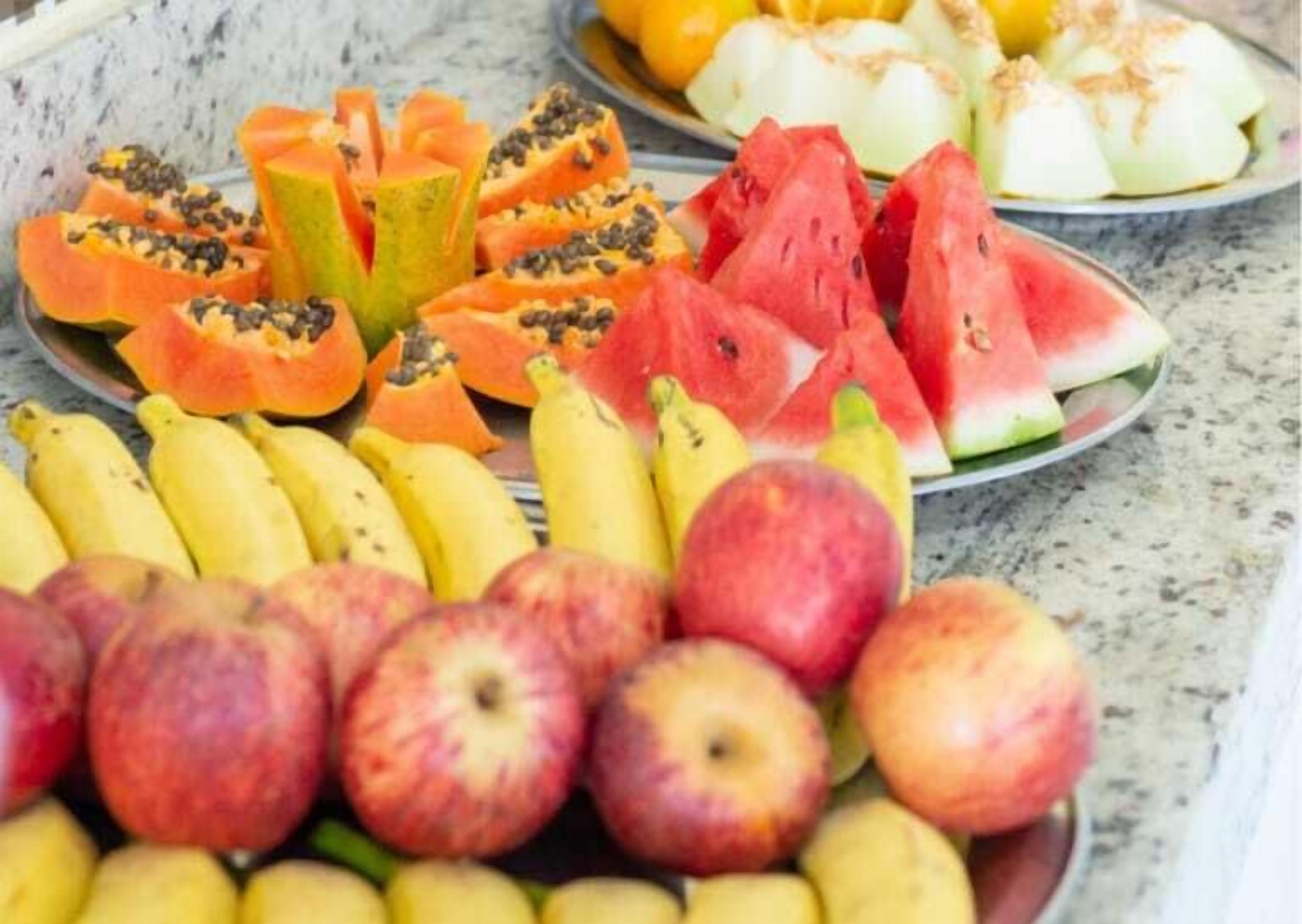 A variety of fruits including apples, bananas, papaya, and watermelon on a marble surface.