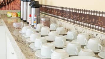 Un ripiano della cucina con diverse tazze e piattini bianchi, una macchina da caffè e un bollitore.