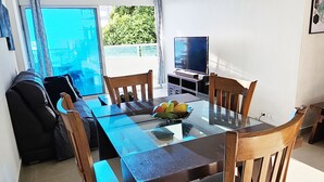 Un comedor con mesa de vidrio y sillas de madera, un sofá y un televisor sobre un mueble bajo.
