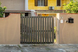 Une entrée fermée par un portail donnant accès à un immeuble dont la façade est de couleur beige, avec un portail en bois et une plaque indiquant le numéro de l’unité.