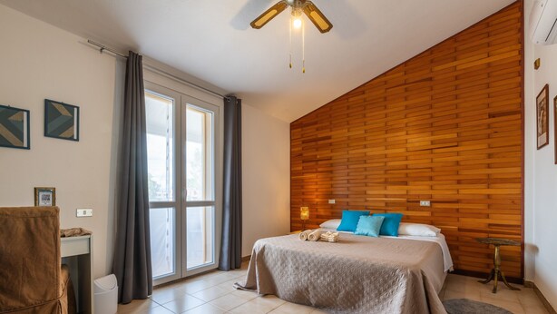 Un dormitorio con cama, escritorio, silla, ventana y ventilador de techo.