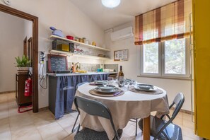 A dining area with a table set for four, a kitchen in the background, and a window with curtains.