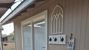 A wooden exterior with a sliding glass door, a welcome sign, and a small porch area with a bench and potted plants. - Charming studio in fabulous Meridian, Idaho with WiFi, AC, Private entry. (Meridian)