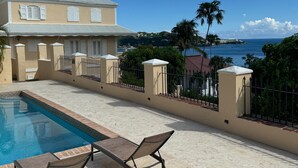 Zona de piscina amb gandules, vista a l'oceà i un edifici amb façana de tons clars i persianes blanques.