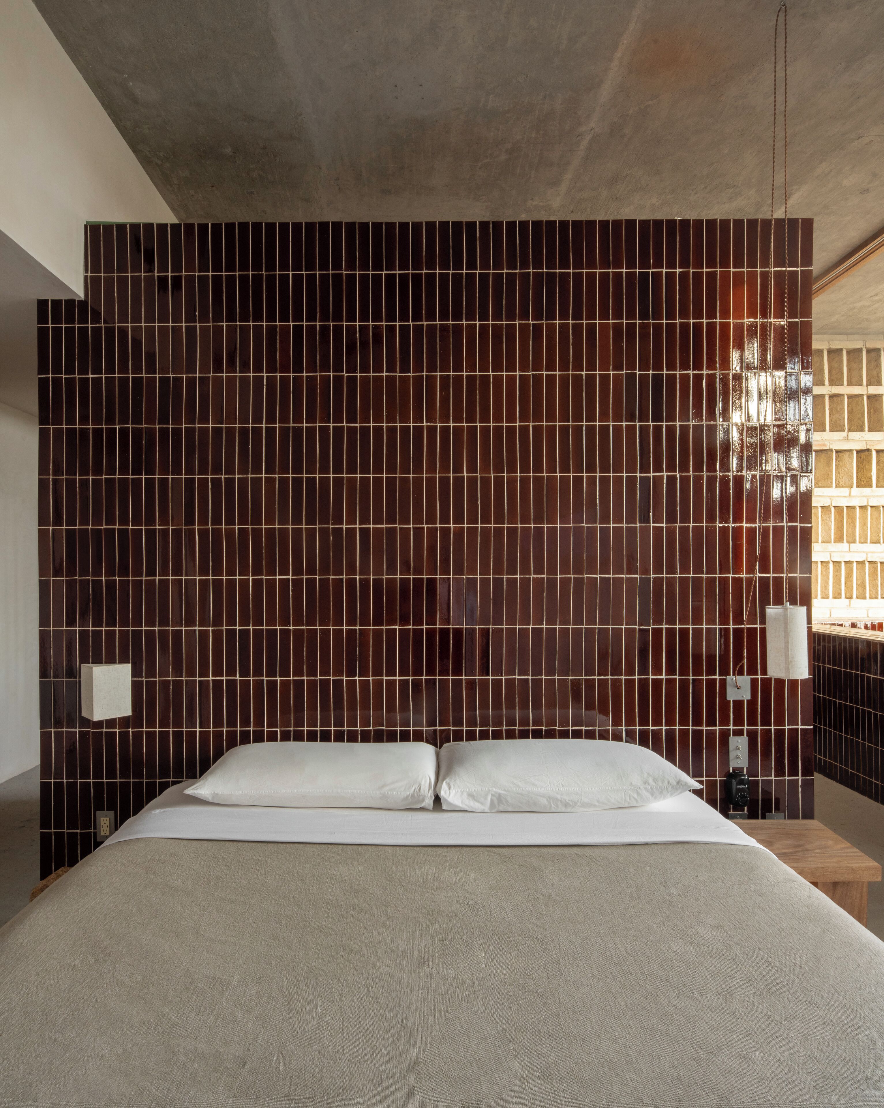 Un dormitorio con una cama grande, cabecera con azulejos, una mesita de noche y un aparador.