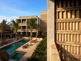 Un resort con piscina, sillas de descanso, palmeras y un edificio de varios pisos con balcones.