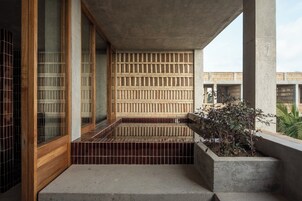 Un edificio moderno con fachada de concreto, puerta de madera y interior con baldosas.