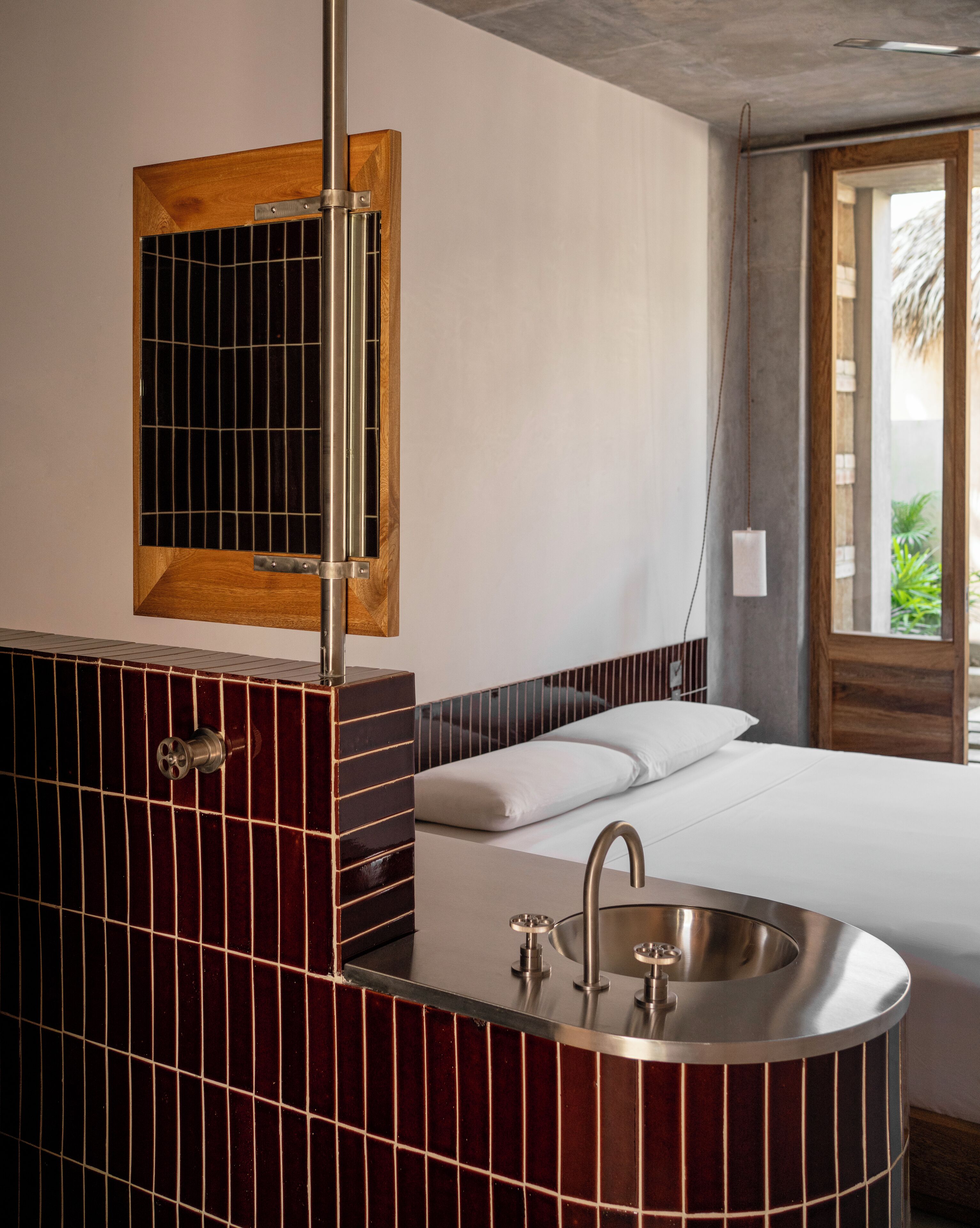 A modern bathroom with a freestanding sink, a wooden-framed mirror, and a bed with white linens.