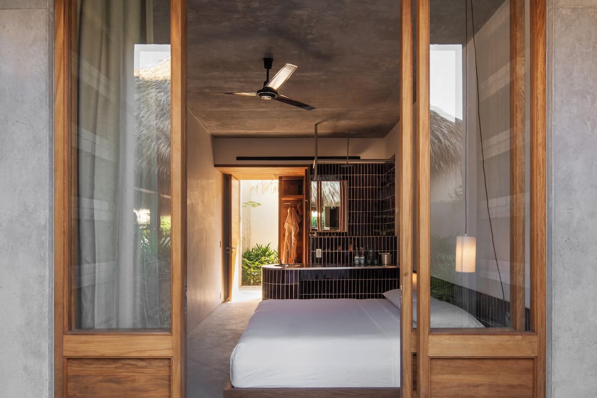A modern bedroom with a large bed, wooden doors, and a ceiling fan.